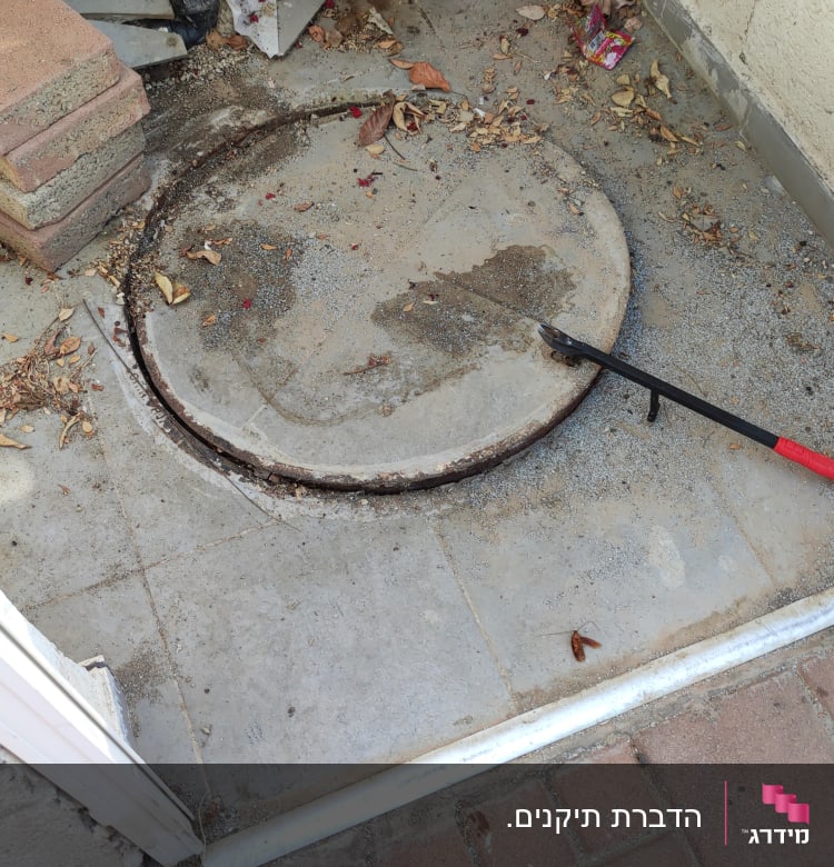 מכסה ביוב עם מוט פתיחה על רצפה מלוכלכת